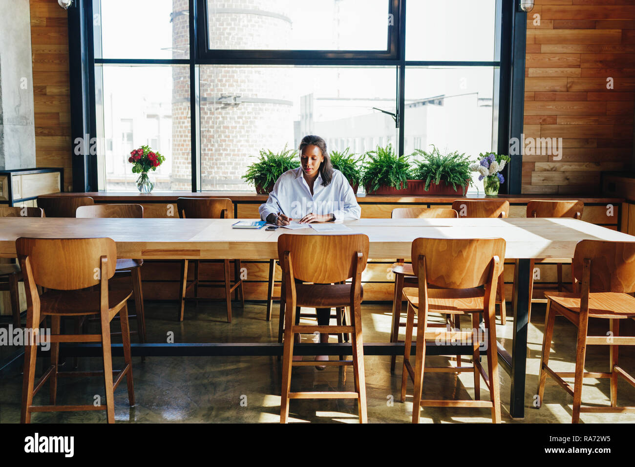Frau sitzt mit einem Schreibtisch, während die Überprüfung der Dateien im Coffee Shop Stockfoto