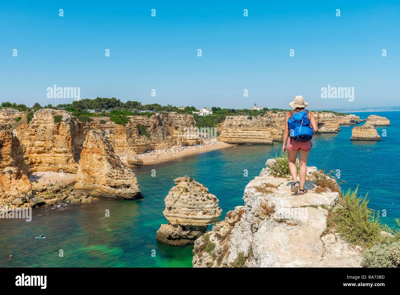 Junge Frau, die auf den Felsen, mit Blick auf das türkisfarbene Meer, Strand Praia da Marinha, Schroffe Felsenküste von Sandstein Stockfoto