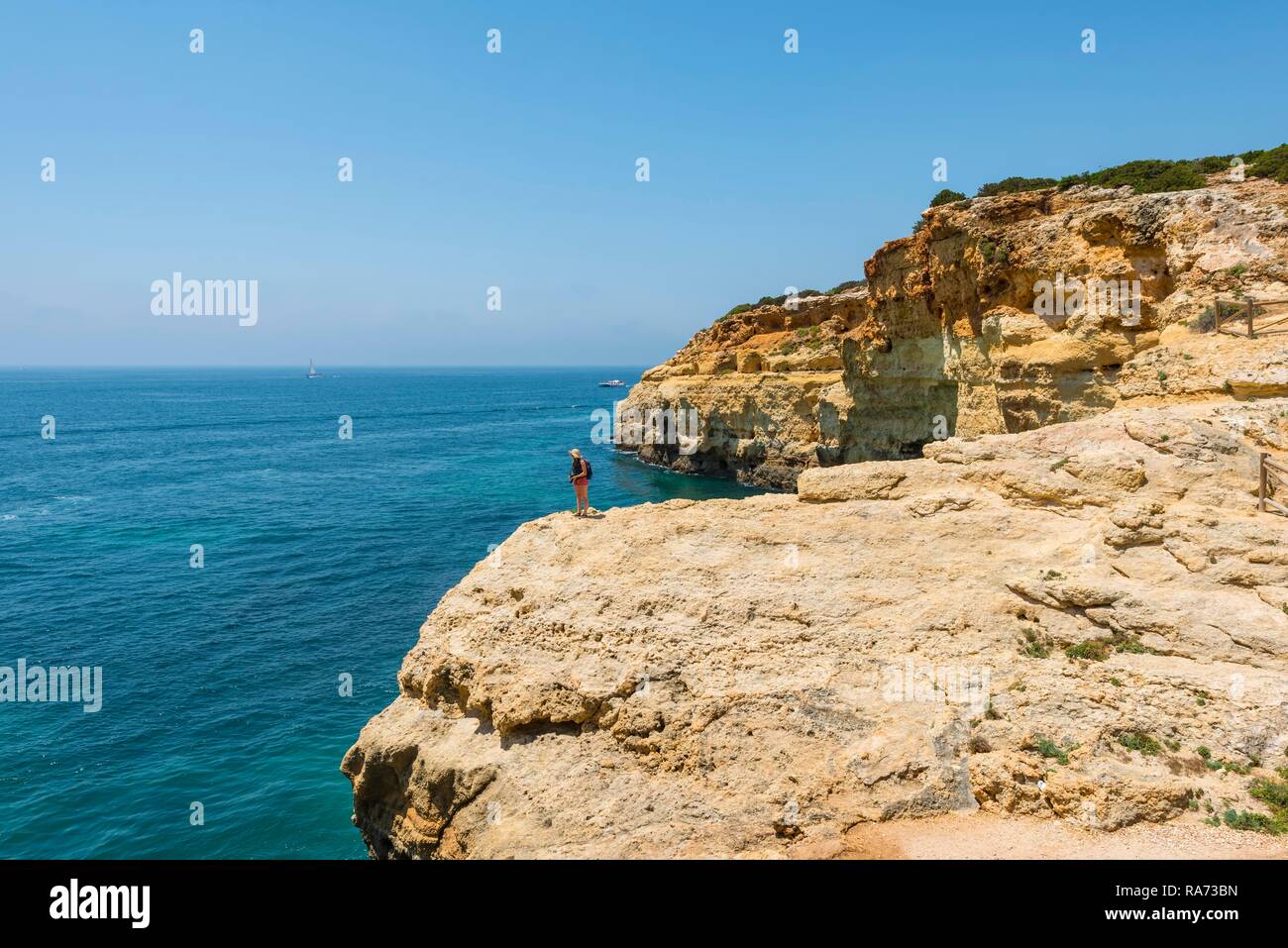 Junge Frau, die auf den Felsen an der Steilküste, mit Blick auf das türkisfarbene Meer, Strand Praia da Marinha, zerklüftete Felsküste aus Sandstein Stockfoto