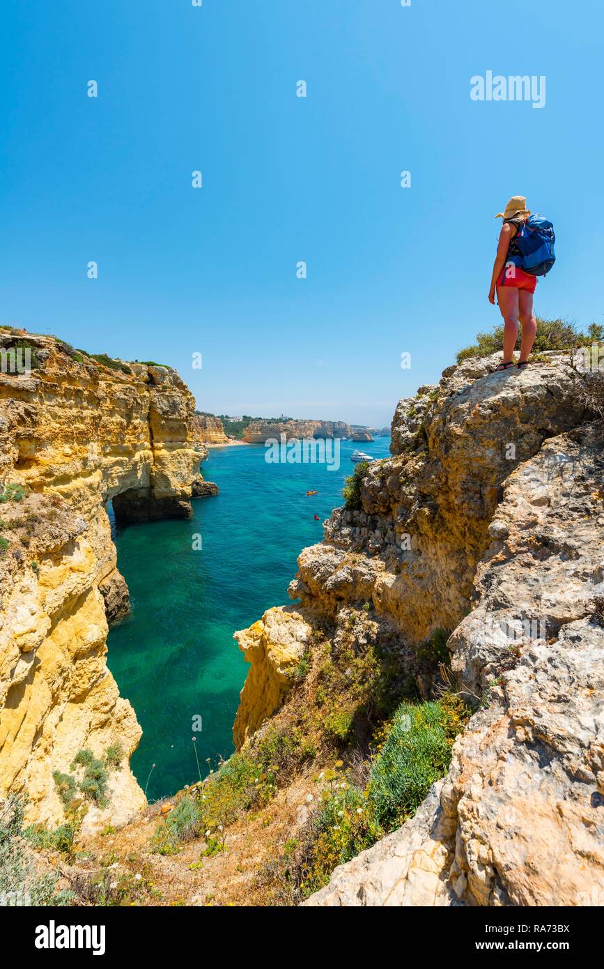 Junge Frau, die auf den Felsen an der Steilküste, mit Blick auf das türkisfarbene Meer, Strand Praia da Marinha, zerklüftete Felsküste aus Sandstein Stockfoto