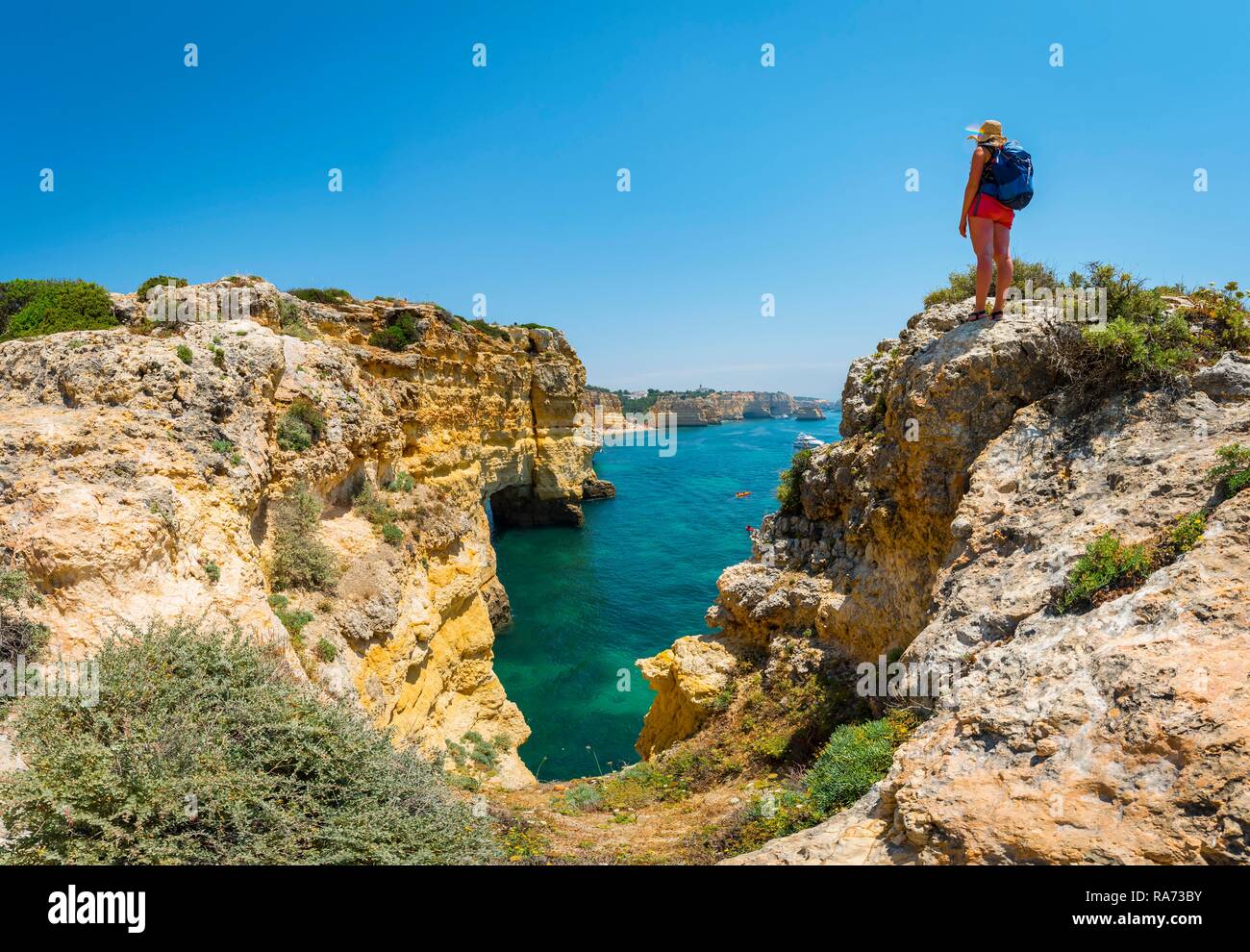 Junge Frau, die auf den Felsen an der Steilküste, mit Blick auf das türkisfarbene Meer, Strand Praia da Marinha, zerklüftete Felsküste aus Sandstein Stockfoto