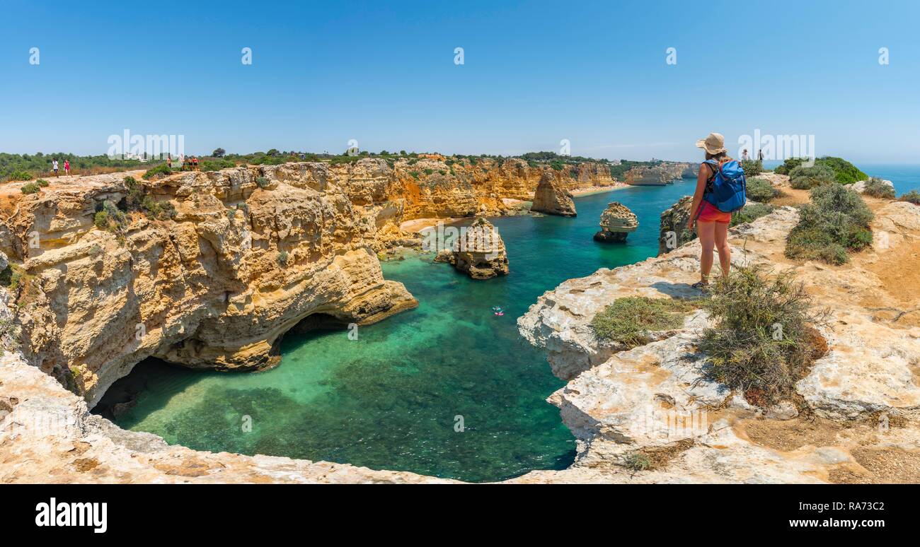 Junge Frau, die auf den Felsen an der Steilküste, mit Blick auf das türkisfarbene Meer, Strand Praia da Marinha, zerklüftete Felsküste aus Sandstein Stockfoto