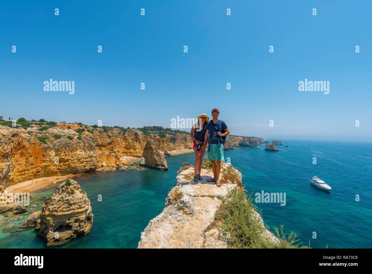 Zwei Touristen stehen auf einer Felsenklippe an der steilen Küste, Strand Praia da Marinha, Schroffe Felsenküste von Sandstein Stockfoto