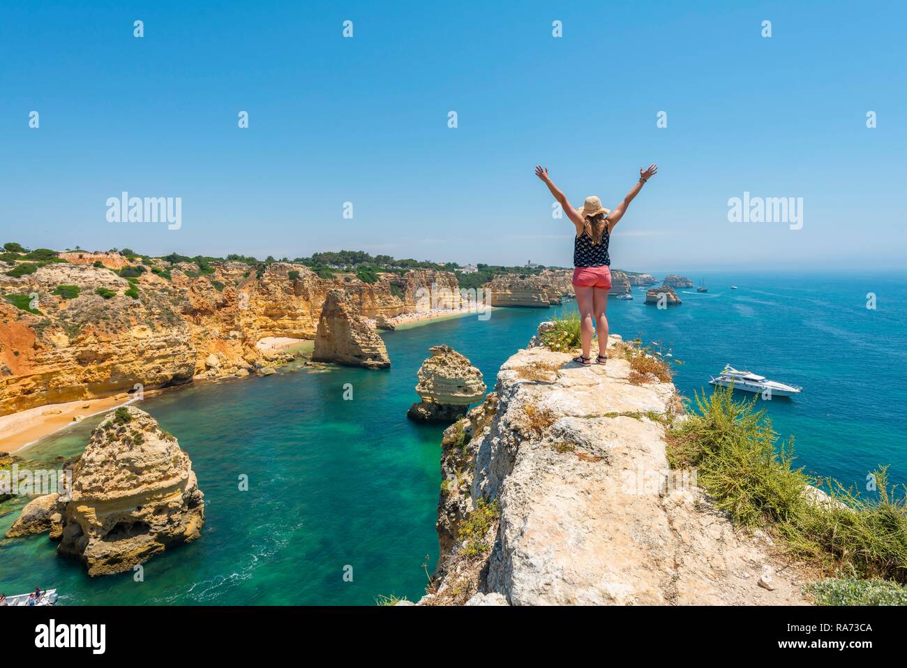 Junge Frau, die auf den Felsen an der Steilküste, streckt die Arme in die Luft, die über Türkis Meerblick, Strand Praia da Marinha. Stockfoto