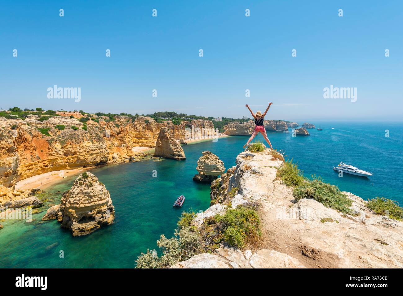Junge Frau auf Felsen an der Steilküste, springt in die Luft, über das türkisfarbene Meer, Strand Praia da Marinha. Stockfoto