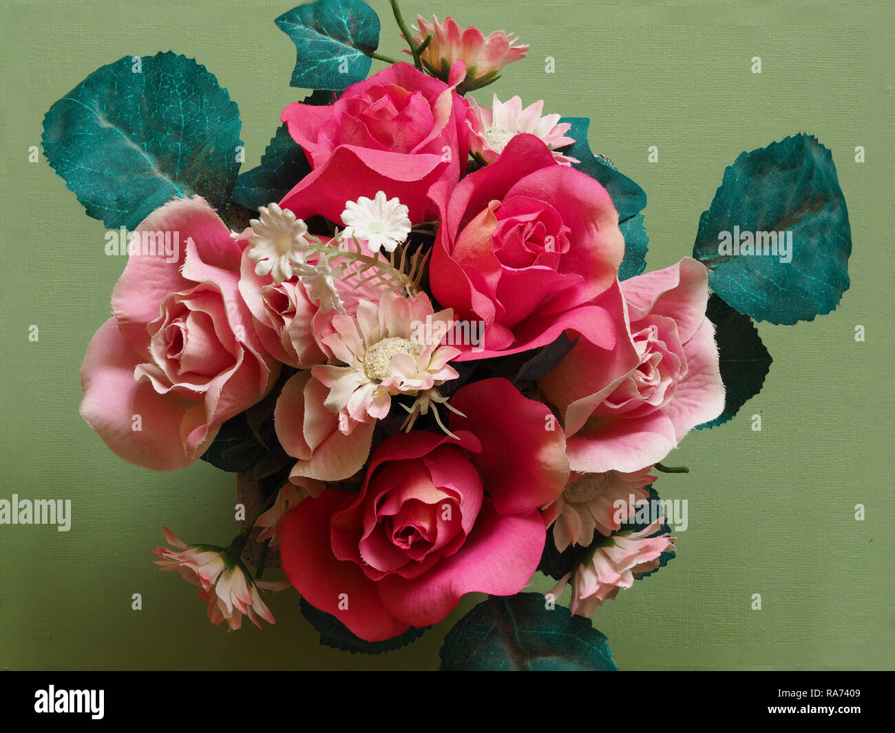 Blumenstrauß aus künstlichen Blumen mit rosa Rosen und grünen Blätter von oben mit einem grünen Hintergrund Stockfoto
