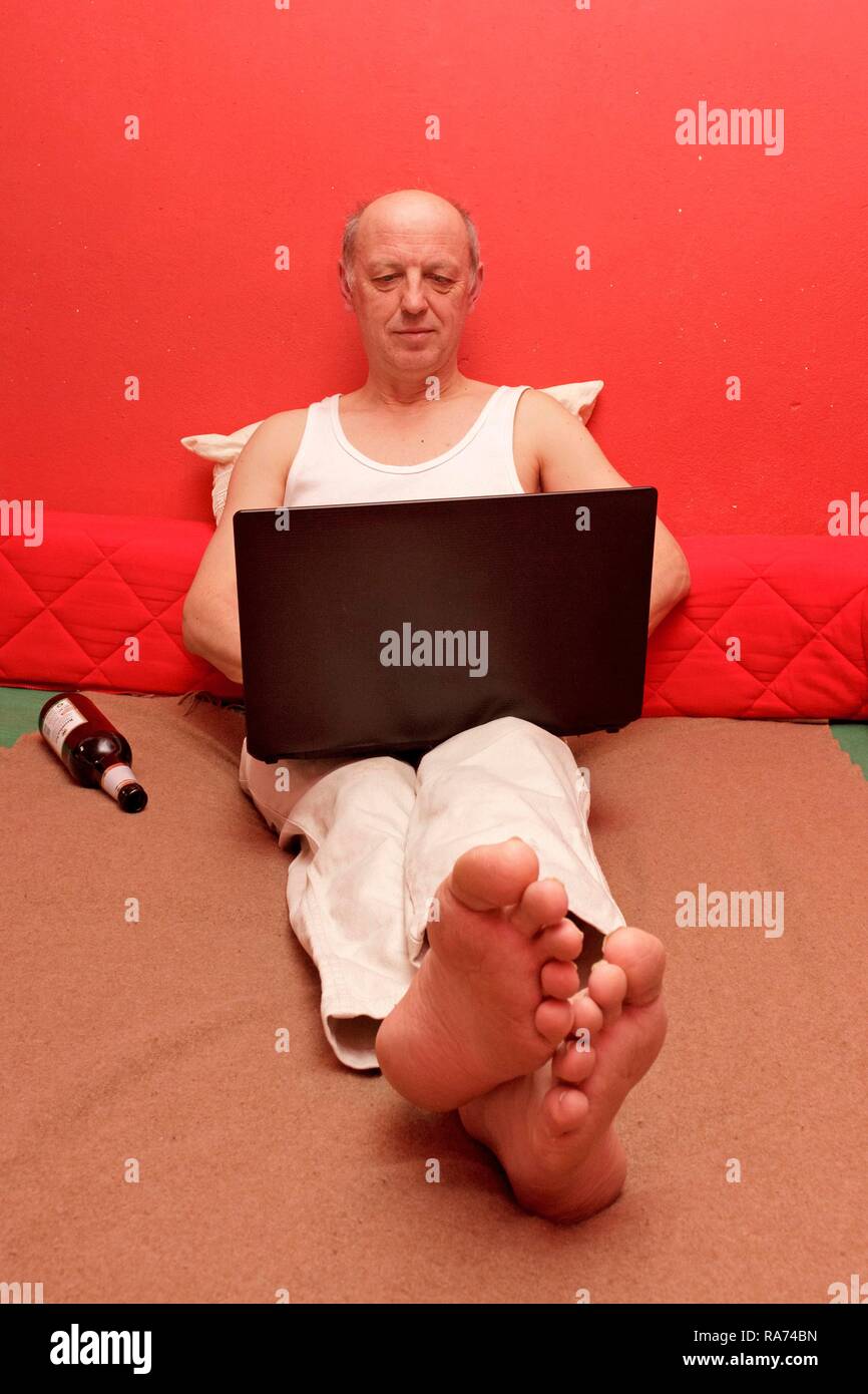Mann im Bett sitzend mit Laptop und Bier Flasche Stockfoto