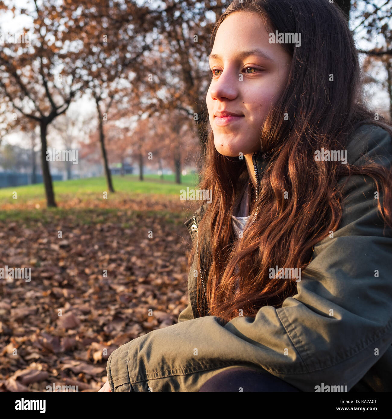 Portrait von hübsches junges Mädchen mit braunen langen Haaren und grüne Jacke, Herbst Hintergrund mit Bäumen und Laub, kopieren Platz für Text Stockfoto