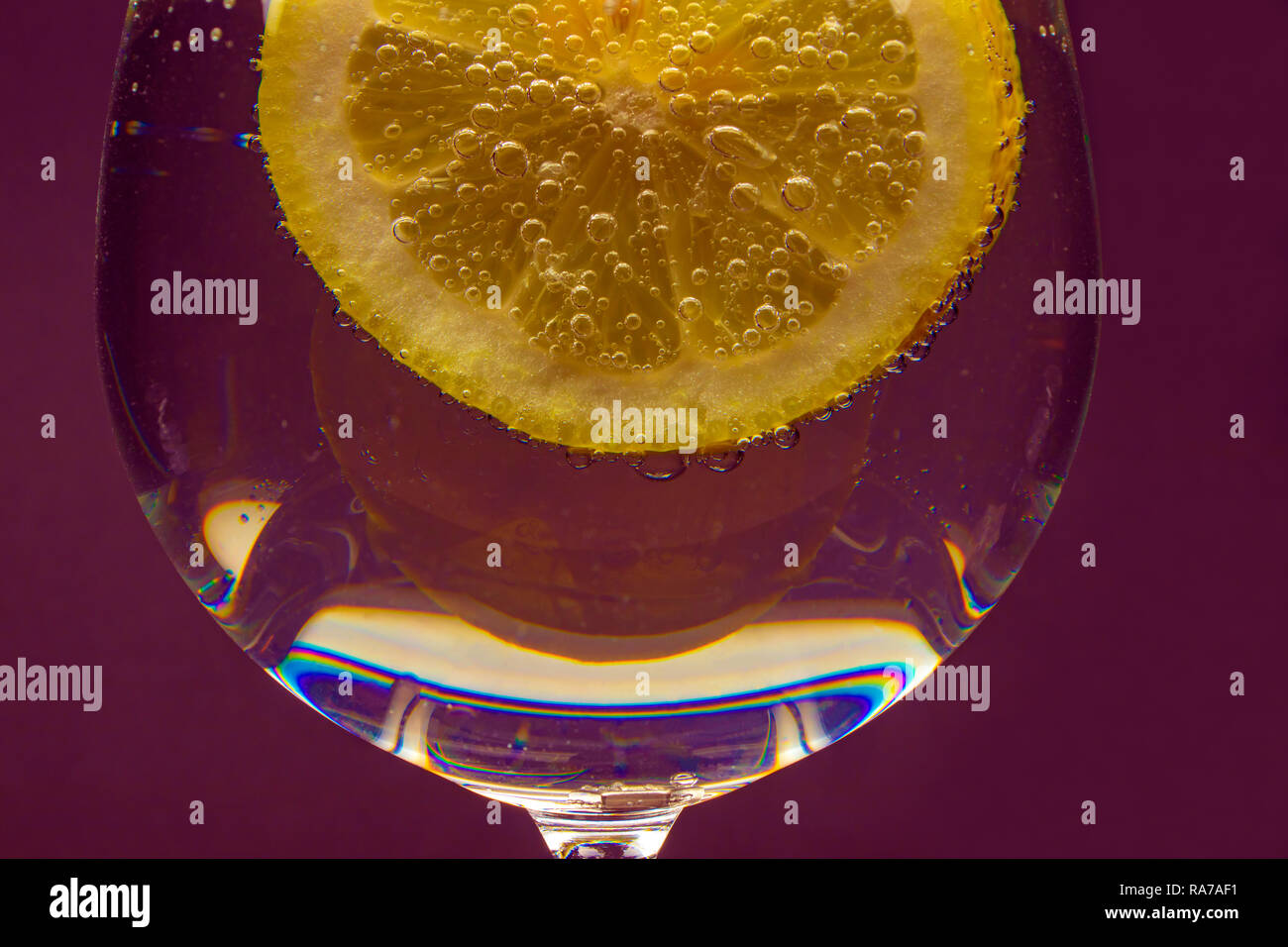 Ein Glas Wasser mit einer Zitronenscheibe mit Blasen auf einem violetten Hintergrund isoliert. Stockfoto