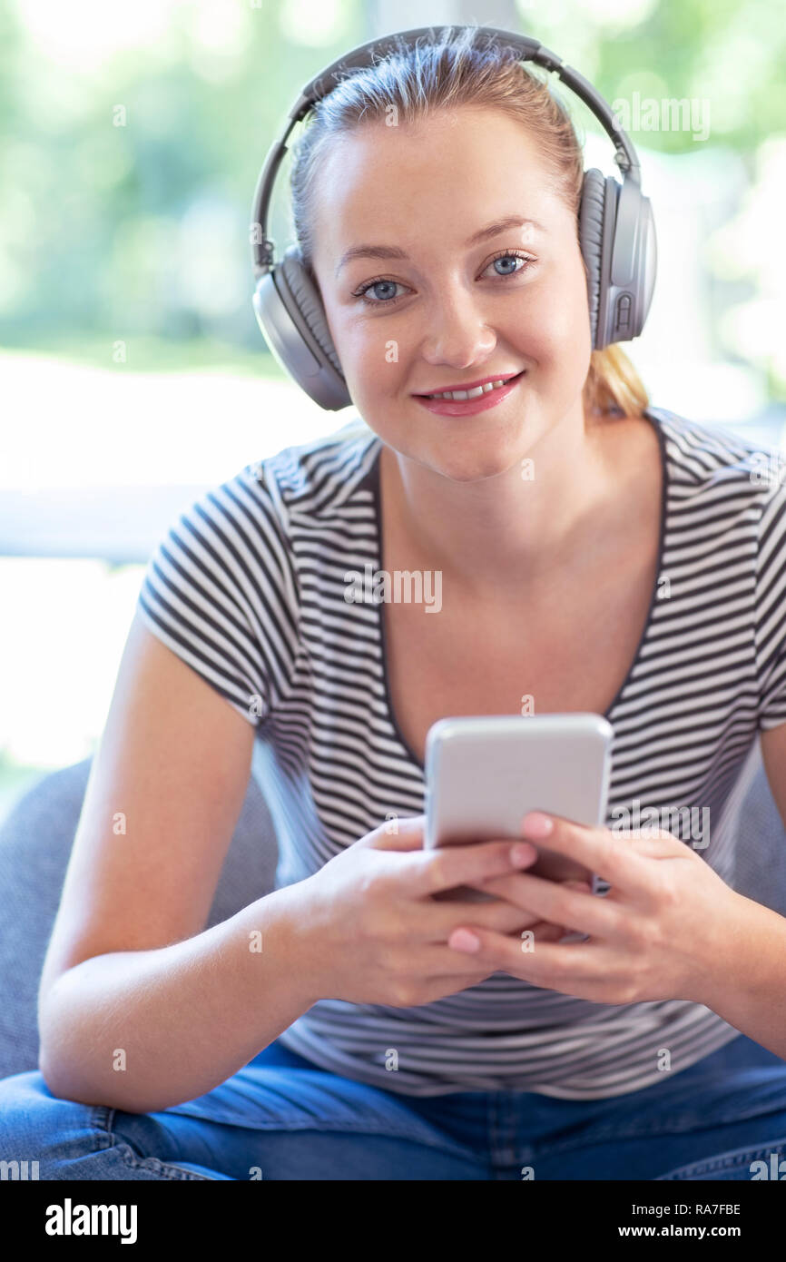 Portrait von Frau zu Hause Streaming Musik vom Mobiltelefon über kabellose Kopfhörer Stockfoto