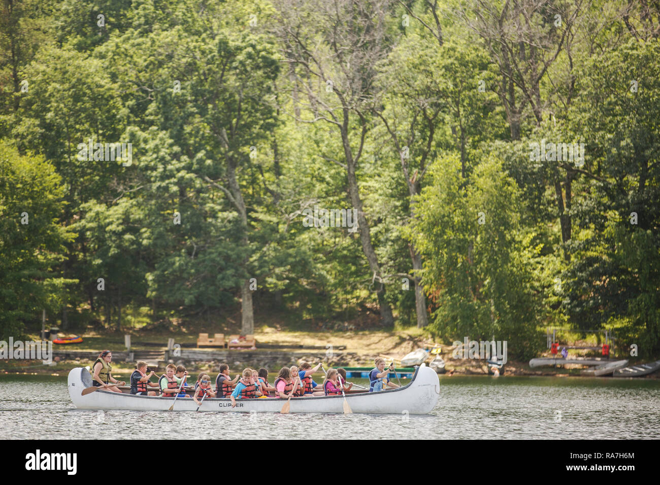 Viele kleine Kinder, die Rettungsanker tragen, füllen ein großes Kanu, das während ihres Sommerlagers in einem See paddelt. Stockfoto