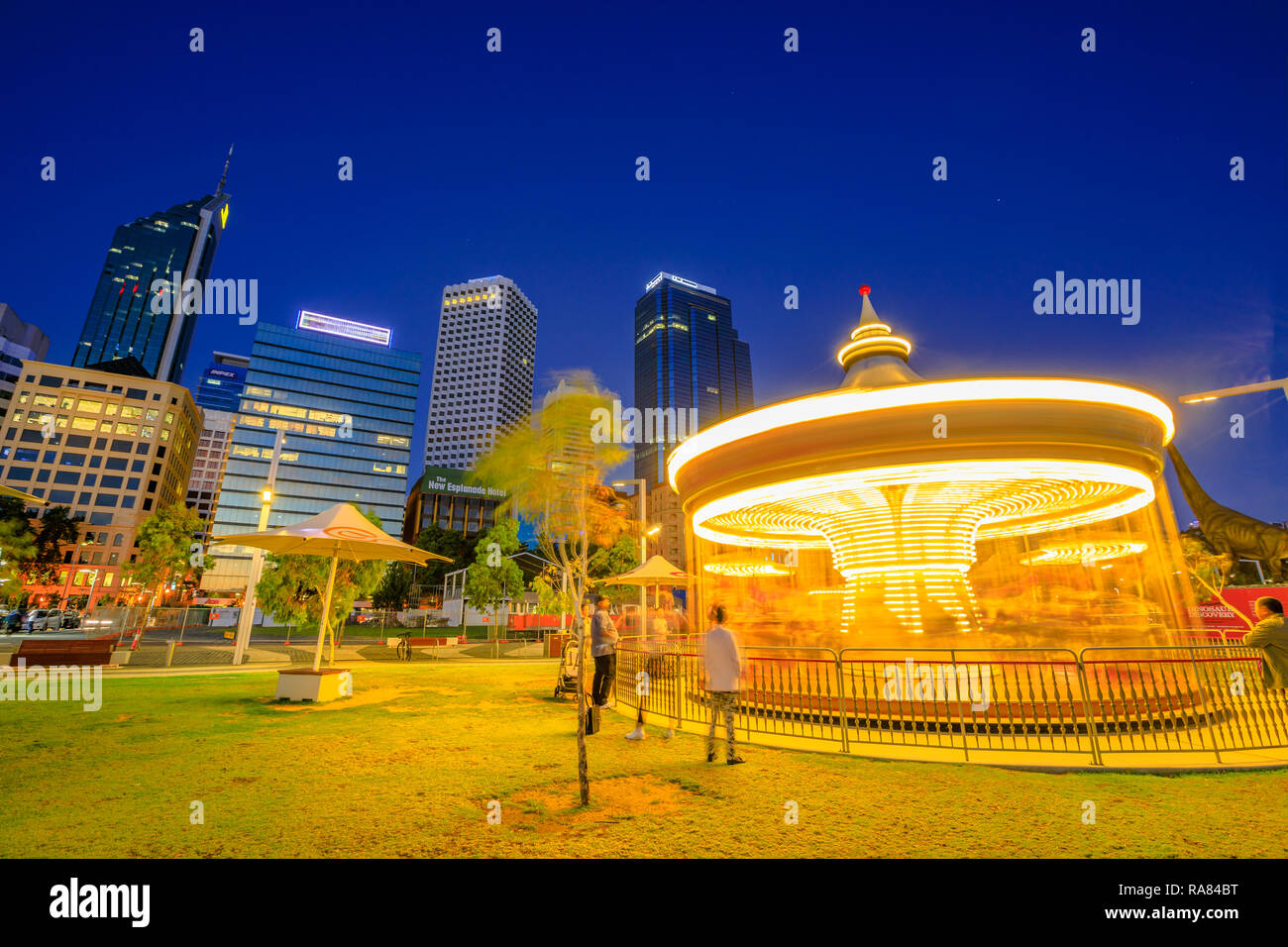 Perth, Western Australia - Jan 6, 2018: Traditionelles venezianisches Karussell bei Nacht beleuchtet läuft schnell in Elizabeth, Kai. Esplanade mit Wolkenkratzern des Geschäftsviertels im Hintergrund. Nacht Szene. Stockfoto