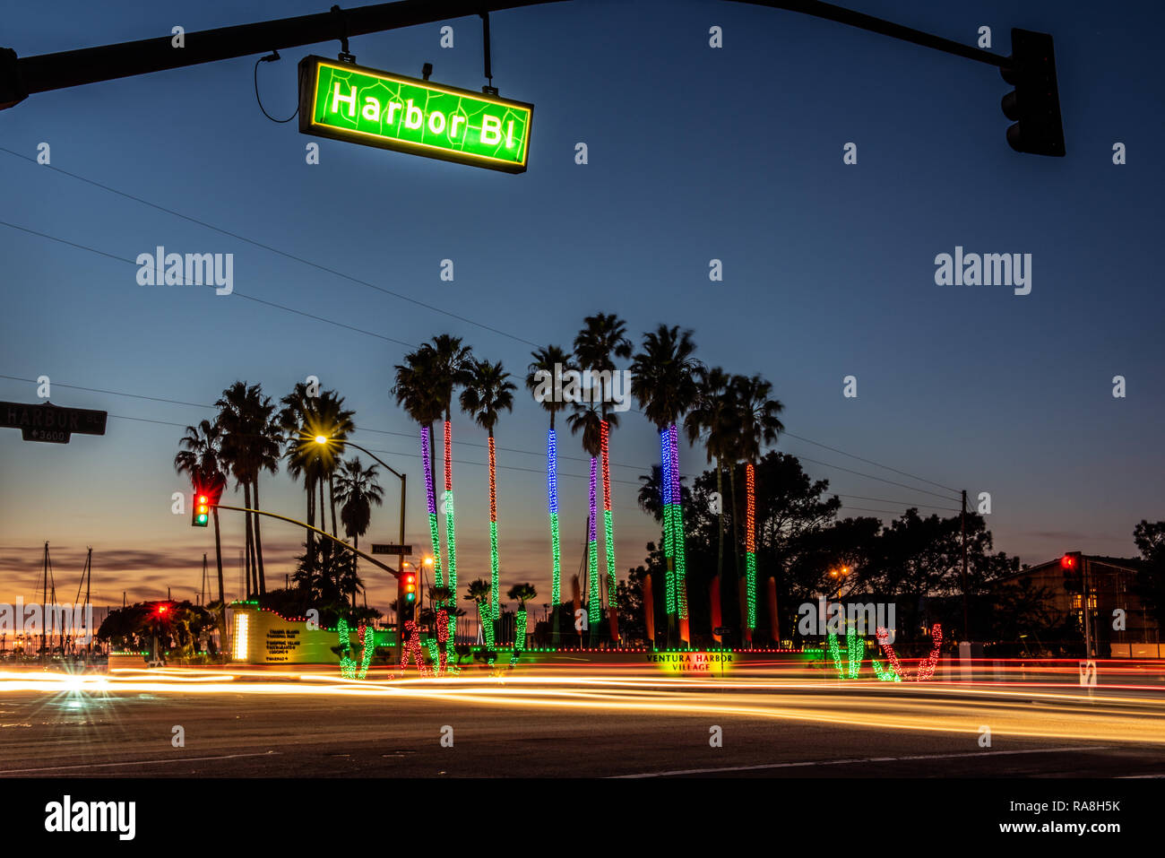Ampel und Streifenbildung Fahrzeuge Kreuz Kreuzung als Sonne hinter Holiday Lights auf Ventura Harbor Bäume am Neujahrstag 2019 in Ventura, C Stockfoto