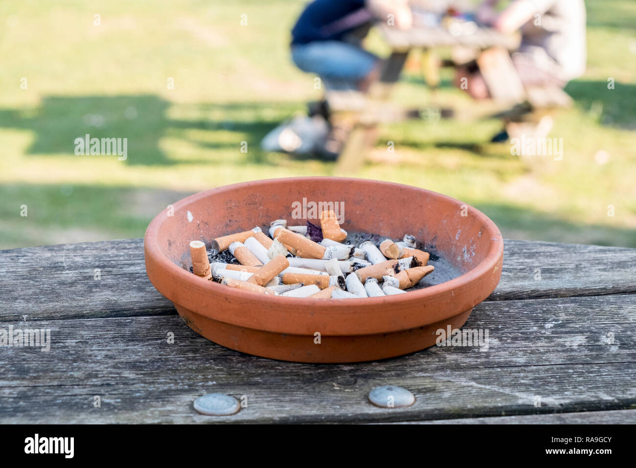 Terrakotta Aschenbecher mit Zigarettenkippen oder fag endet an einem Tisch draußen, England, Großbritannien Stockfoto