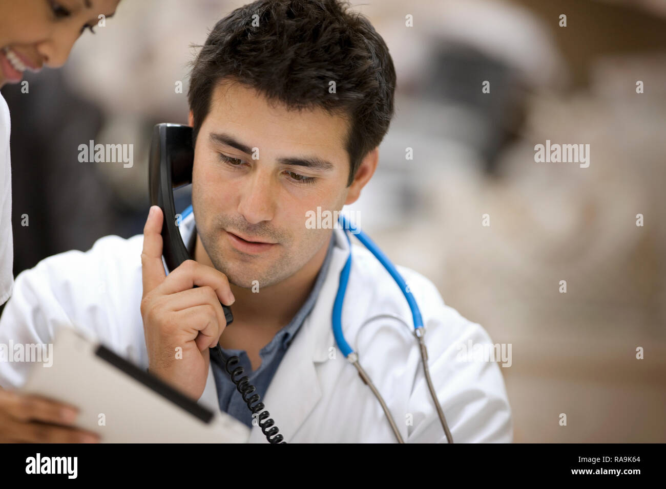Junge männliche Arzt am Telefon, während in der Zwischenablage, die eine junge Krankenschwester ihm zeigt. Stockfoto