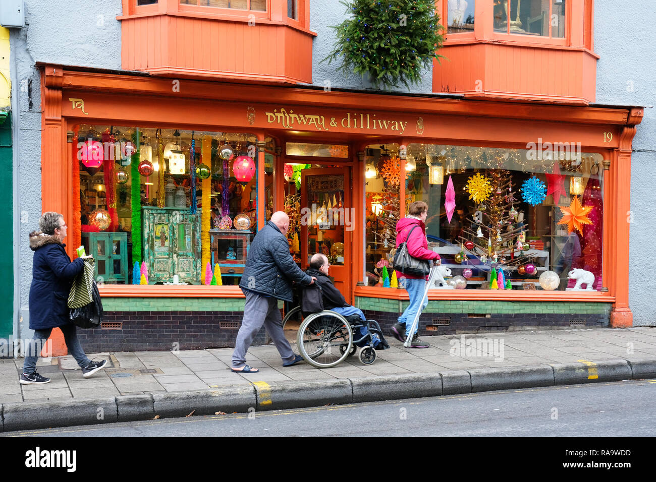 Behinderte Person in einem Rollstuhl vor einem New Age shop, Glastonbury, Somerset, Großbritannien - Johannes Gollop geschoben Stockfoto