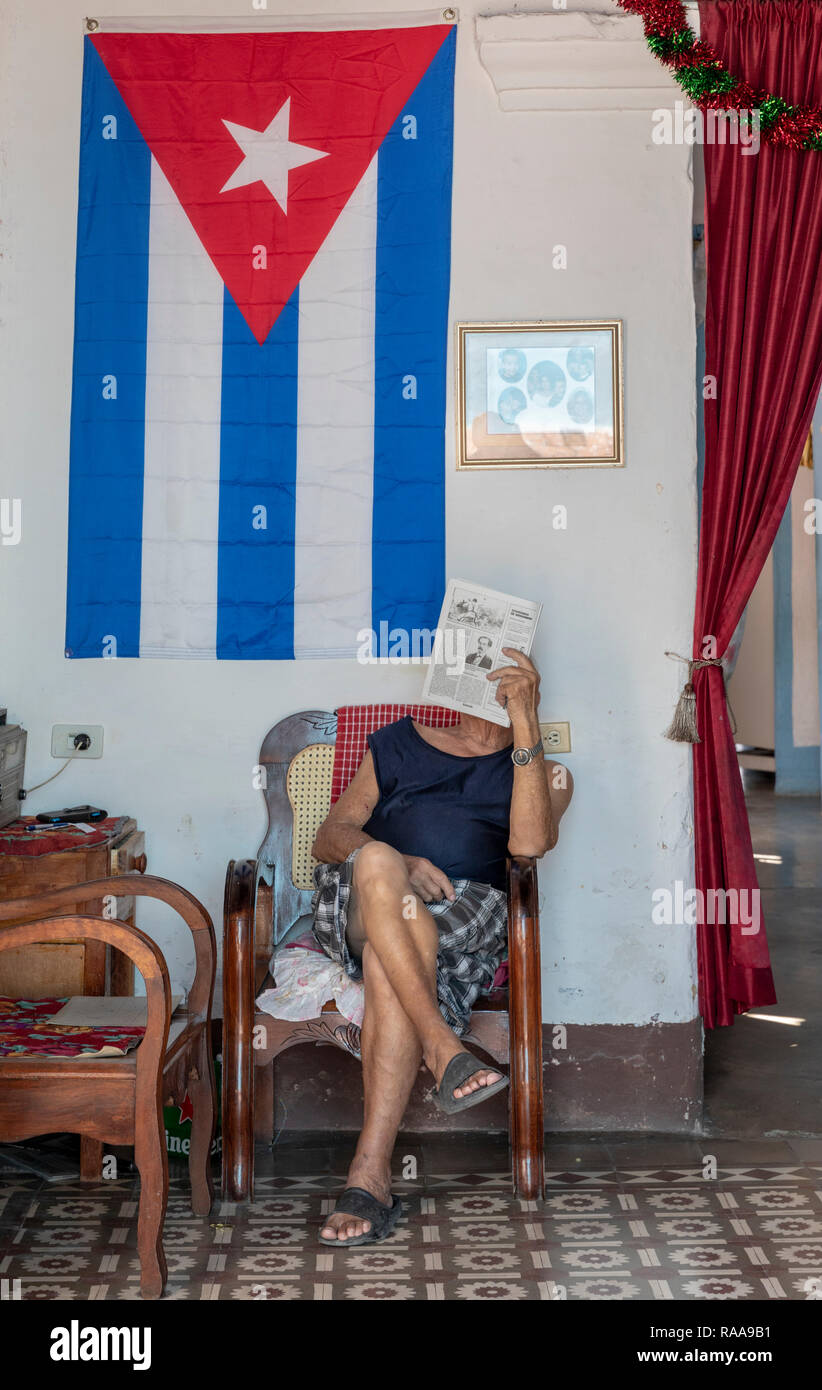 Mann lesen Zeitung unter kubanischer Flagge, Calle Real, Trinidad, Kuba Stockfoto