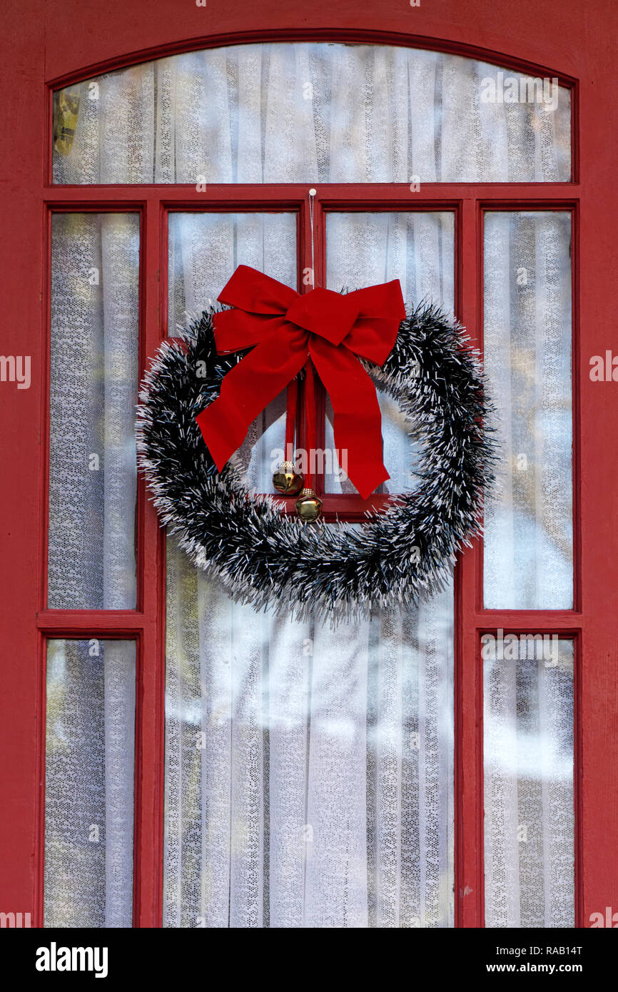 Rote und Grüne Weihnachten Kranz Aufhängen an einer Glastür mit einem roten Rahmen aus Holz Stockfoto