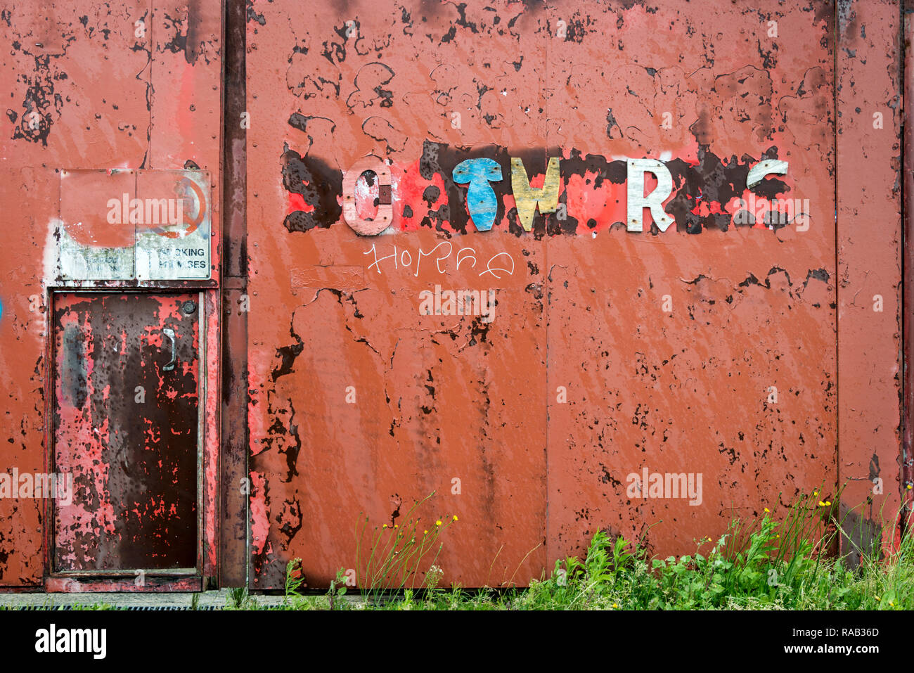 Ein Rot lackiertes Metall Wand mit den Resten der Wörter in bunten gebrochene Buchstaben angebracht Stockfoto