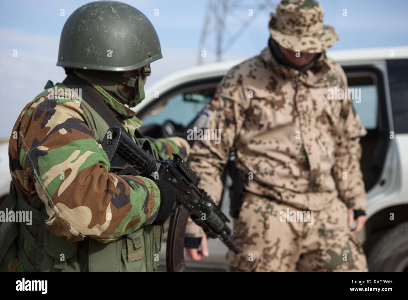 Eine Zeravani Soldat sorgt für Sicherheit auf einen deutschen Trainer während eines simulierten Fahrzeug und Person suchen bei Bnaslawa, Irak, Jan. 26, 2017. Deutschland ist einer von über 60 Koalitionspartnern, die Teil der Combined Joint Task Force - inhärenten Building Partner Kapazität mission Willen zur Ausbildung irakischer Sicherheitskräfte gewidmet. Combined Joint Task Force-Operation inhärenten Lösen, die globale Koalition zu besiegen ISIL im Irak und in Syrien. Stockfoto