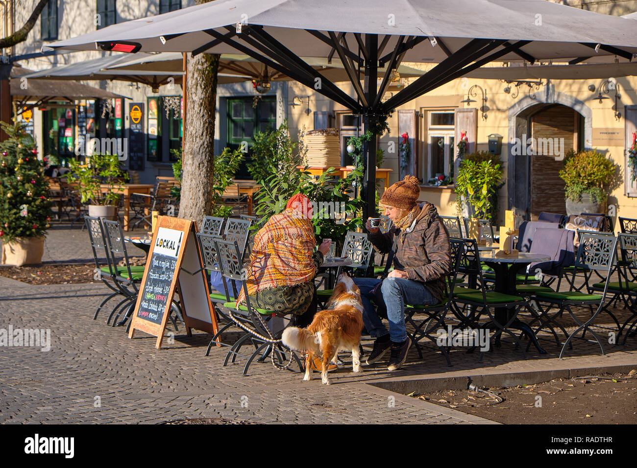 Auf einen Regen sonnigen Wintertag, Personen außerhalb sitzen auf Cafe Terrasse Alle gebündelt einen Drink mit Hund genießen Sie beobachten Stockfoto