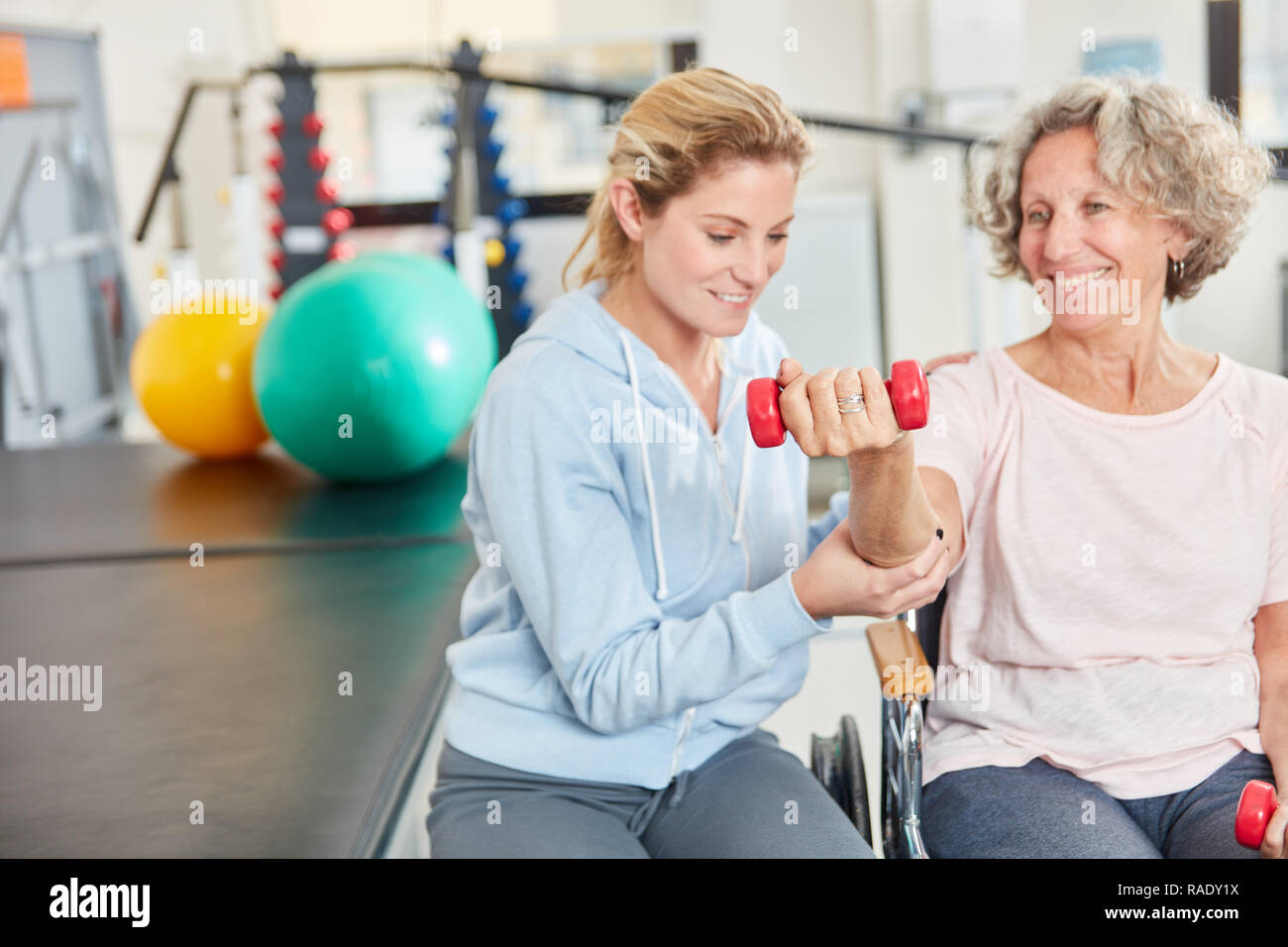 Physiotherapeut unterstützt ältere Frau mit hanteltraining im rehab Stockfoto
