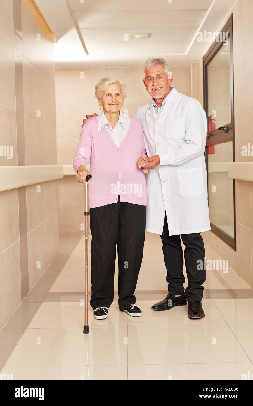 Arzt unterstützt eine gebrechliche ältere Frau mit Stock in der Reha Klinik Stockfoto