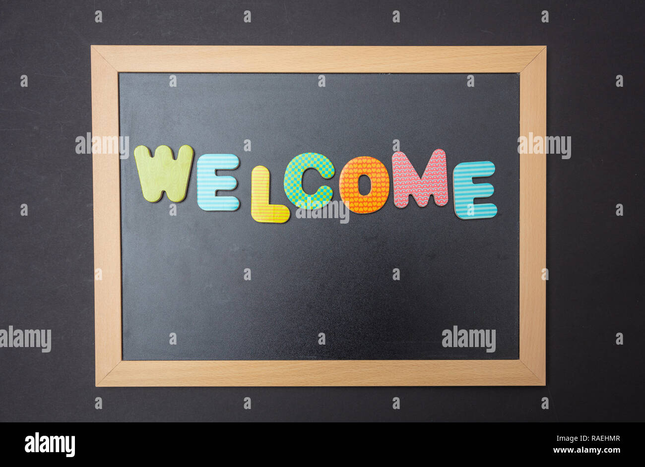 Willkommen. Vorstand mit schwarzem Rahmen, Text Willkommen in bunten Buchstaben, schwarze Wand Hintergrund Stockfoto