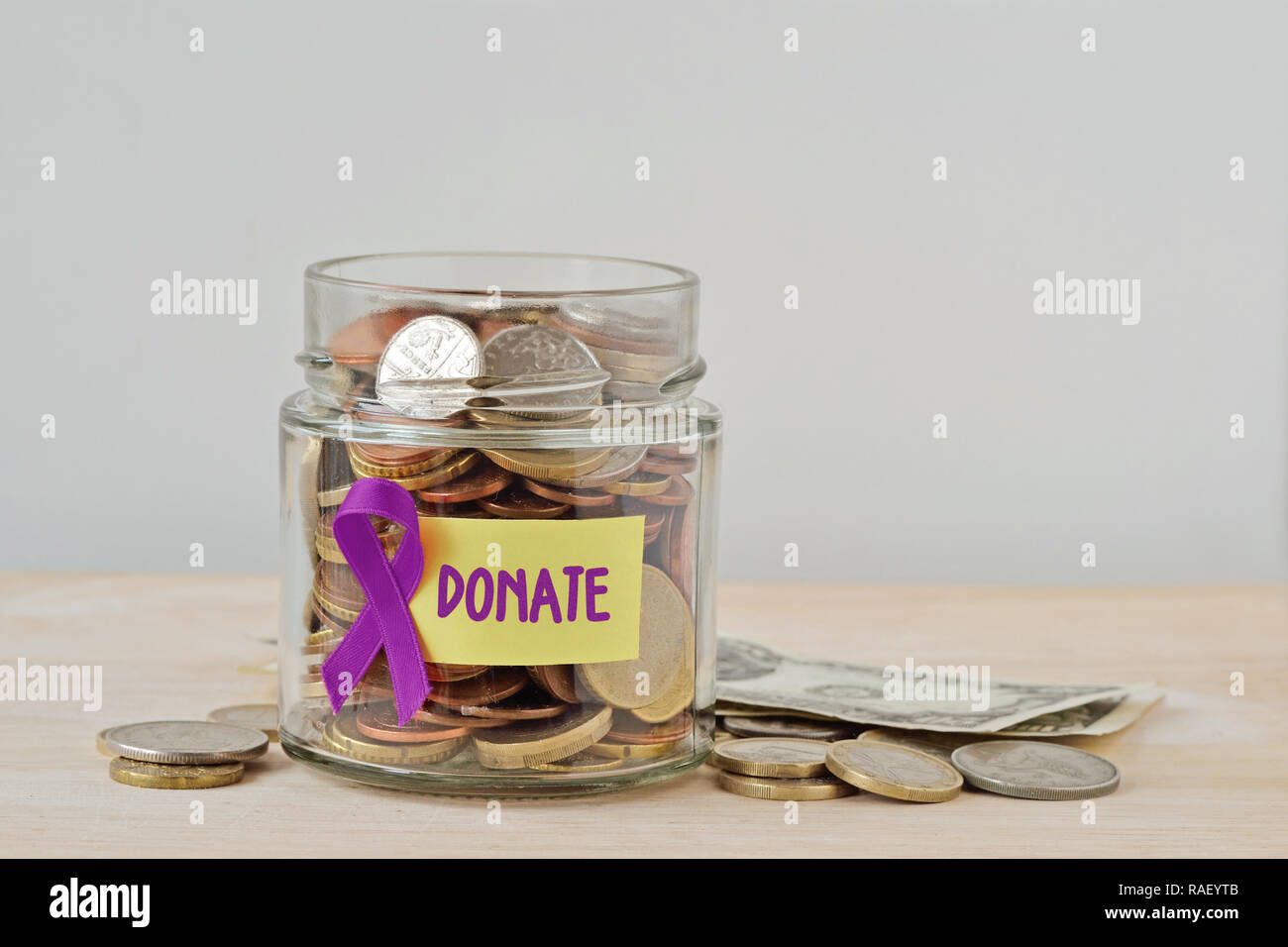 Geld jar voller Münzen mit violetten Band und Label Spenden-Konzept von Alzheimer, Bauchspeicheldrüsenkrebs, Epilepsie, Lymphom Nächstenliebe und resea Stockfoto