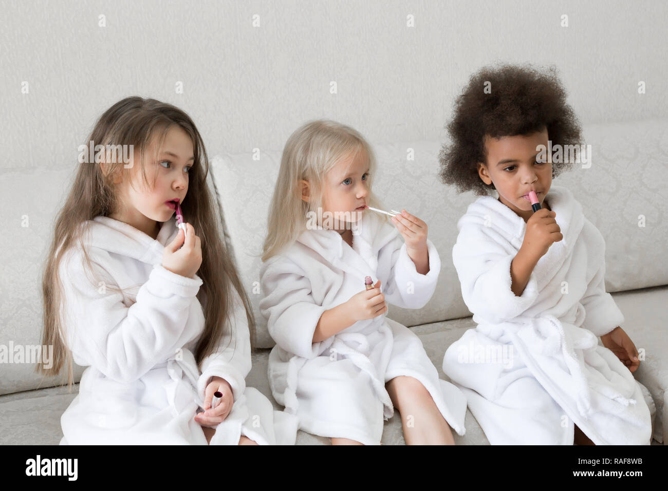 Drei kleine Mädchen in weißen Kitteln nach einer Dusche spielen mit Make-up  Ihren Lippen Farbe mit roten Lippenstift Stockfotografie - Alamy