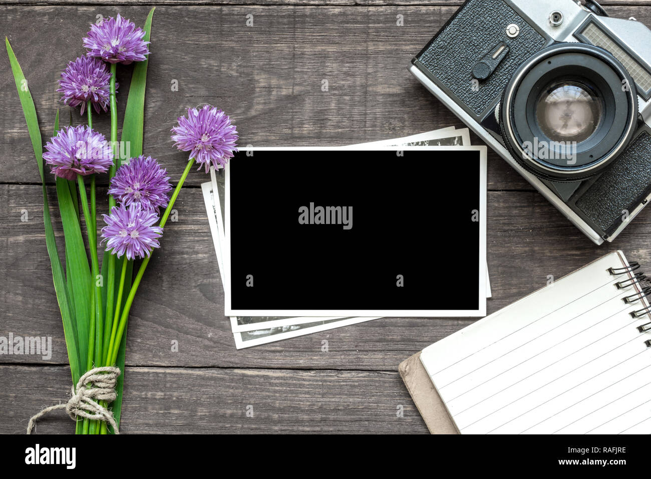 Vintage Retro Kamera mit leeren Bilderrahmen, lila Wildblumen und gesäumt von Notebook mit rustikalen Holzmöbeln Hintergrund. Mock up. top View Stockfoto