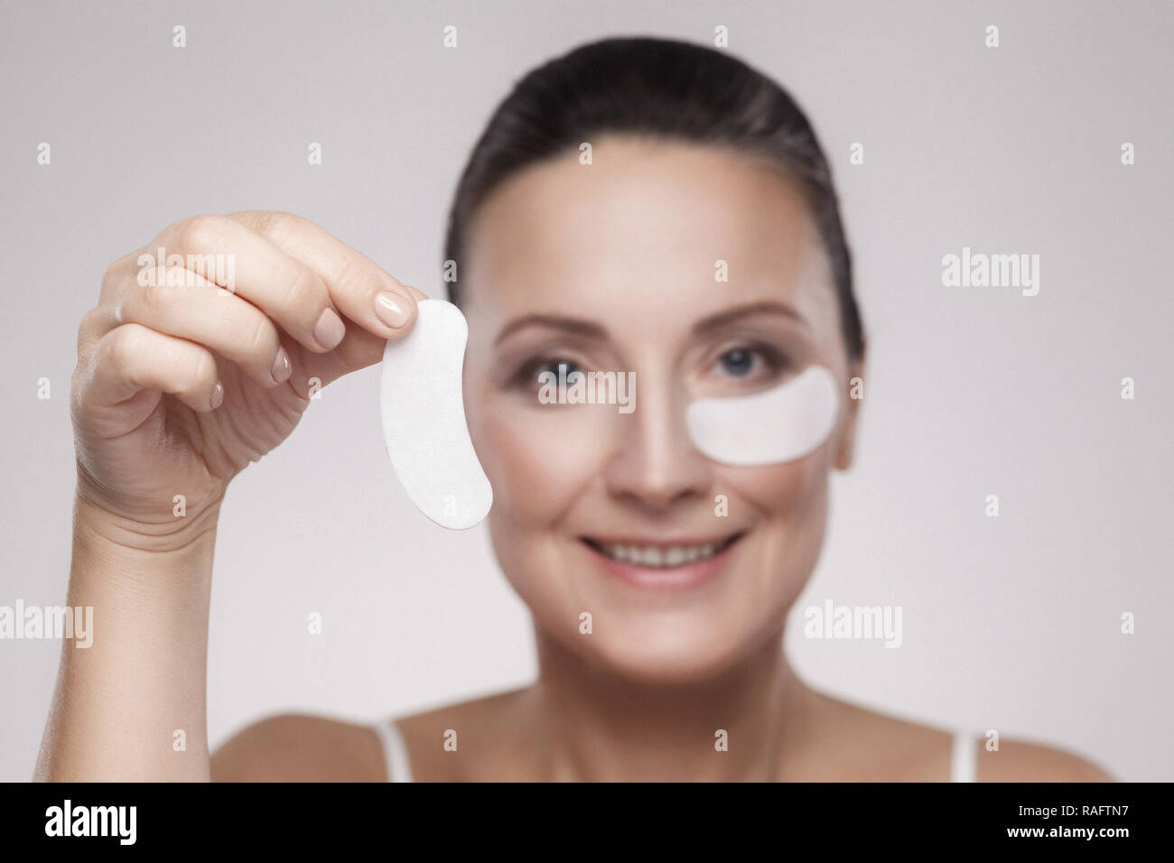 Patches in den Augen. Schöne Frau mittleren Alters mit perfekter Haut weiße Hydrogel Patches mit lifting Anti-falten Kollagen Wirkung, grau backgro Stockfoto