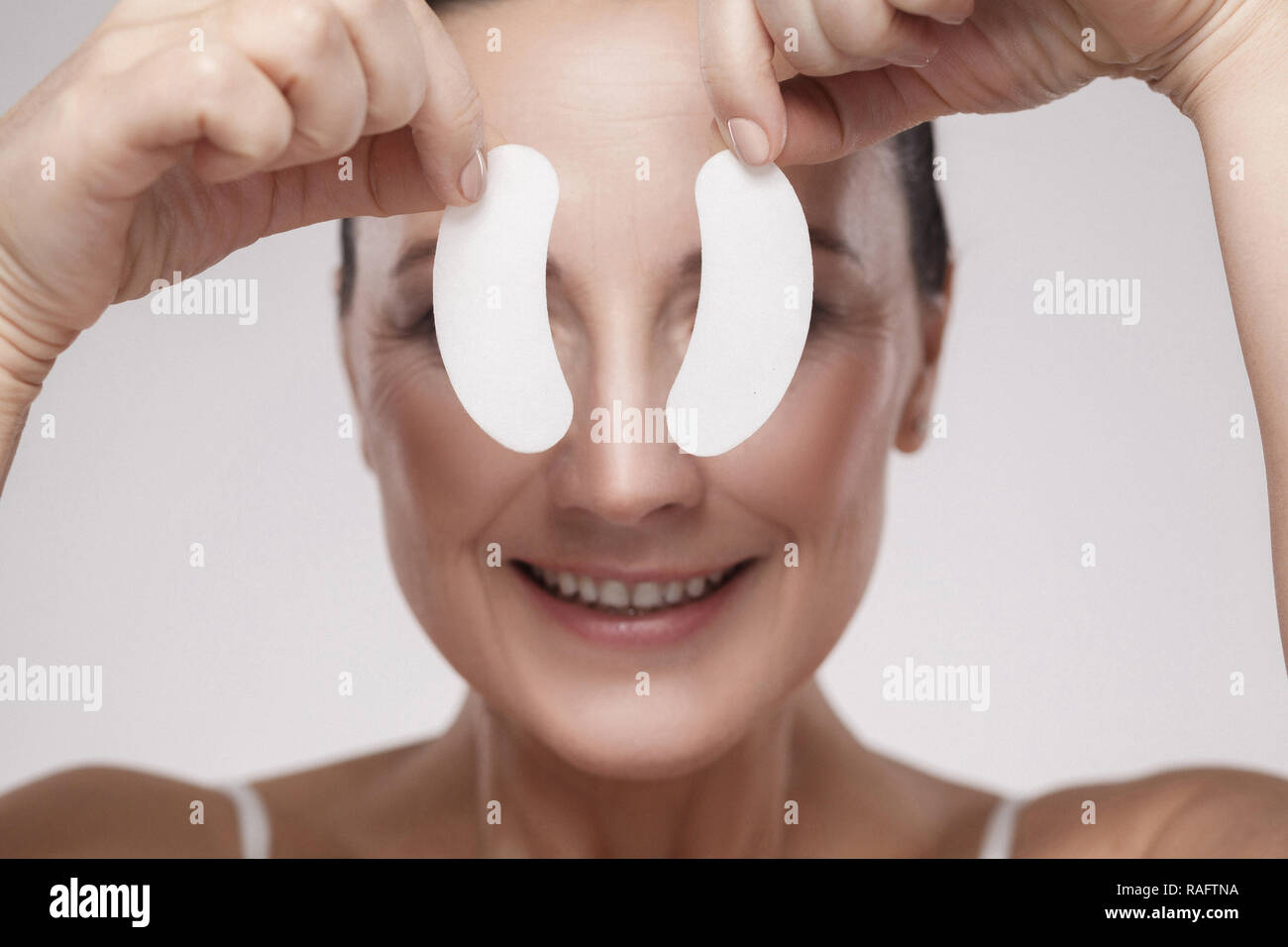Patches in den Augen. Schöne Frau mittleren Alters mit perfekter Haut weiße Hydrogel Patches mit lifting Anti-falten Kollagen Wirkung, grau backgro Stockfoto