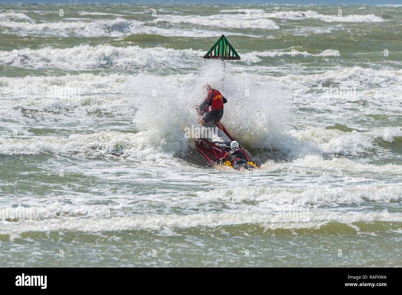 Zwei Rettungsschwimmer hit eine große Welle, wie Sie das rauhe Meer auf einem Jetski oder Wassermotorrädern auf West Wittering Strand, in der Nähe von Chichester, West Sussex, UK eingeben Stockfoto