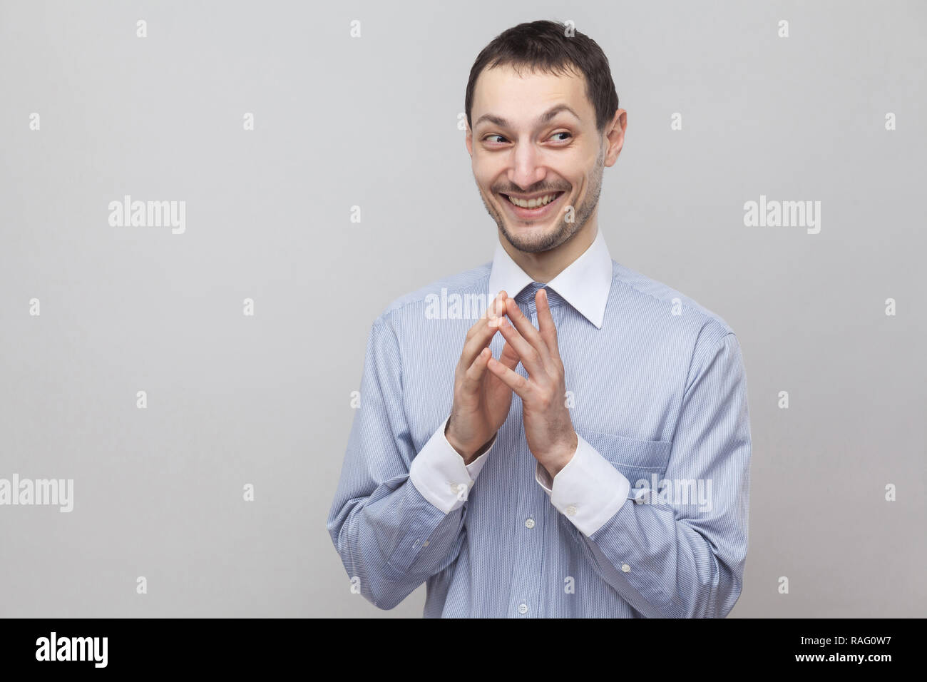 Portrait von lustigen toothy Smiley stattlichen Borste Geschäftsmann in klassischem Hellblau Shirt stehen und weg schauen mit gerissen. indoor Studio sh Stockfoto