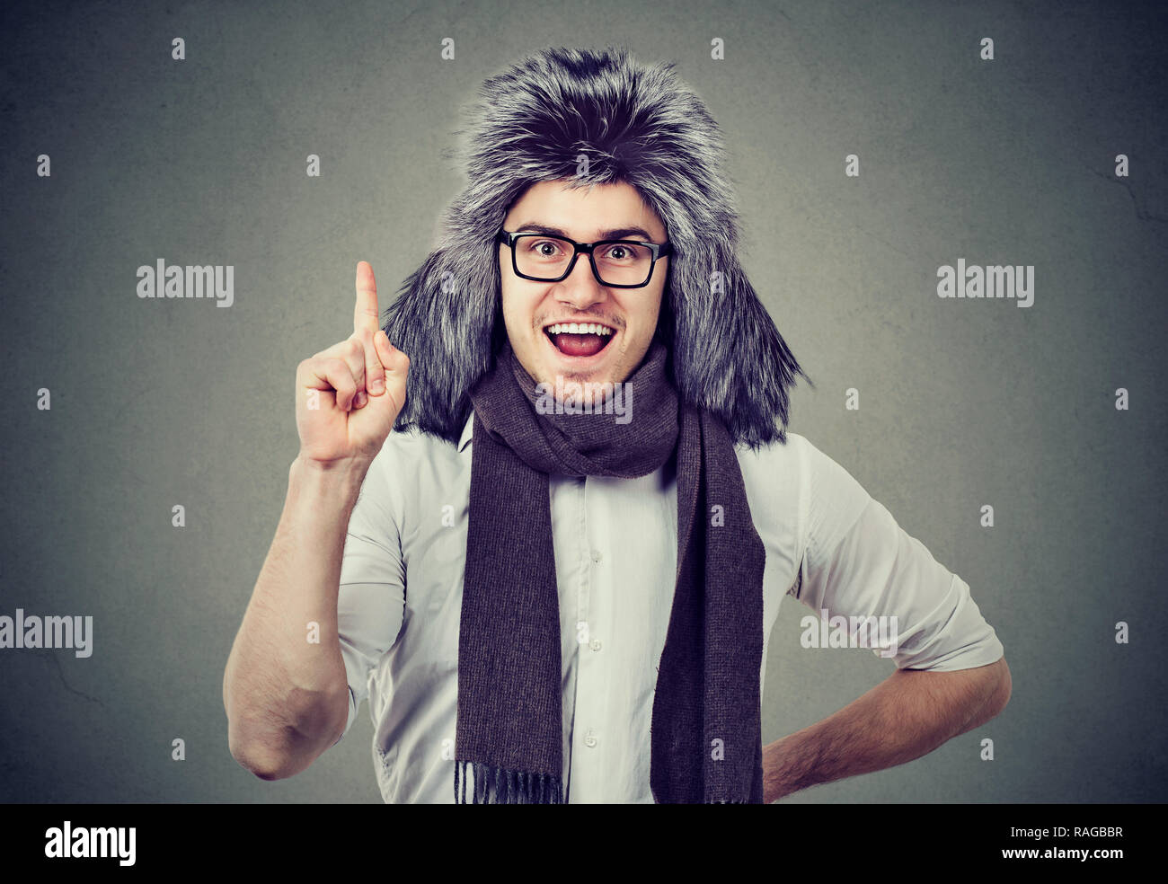 Lächelnd aufgeregt mann im winter Hut und Brille halten Sie einen Finger in der Aufregung an Kamera suchen Stockfoto