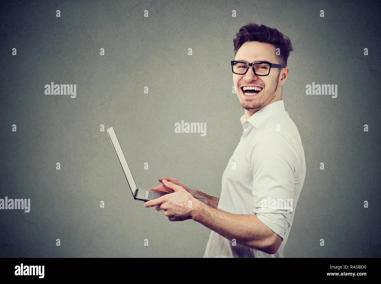 Seitenansicht der glücklichen erwachsenen Mann in Gläsern und weißes Hemd mit modernen Laptop auf grauem Hintergrund Stockfoto