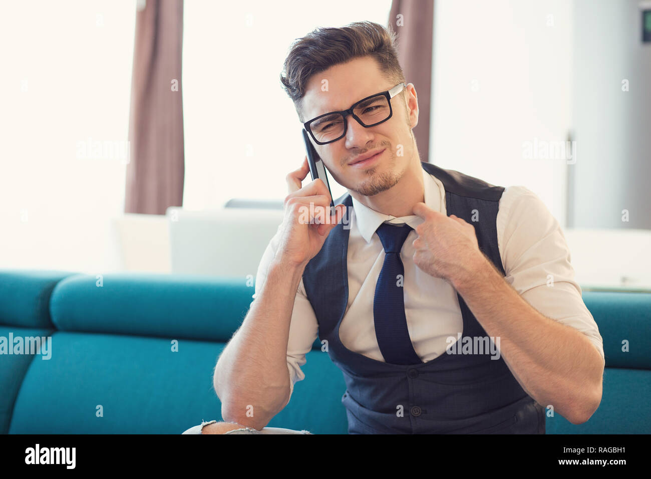 Mann in Gläser, ängstlich, während Sie telefonieren und stirnrunzelnd auf der Couch in der modernen Apartment Stockfoto