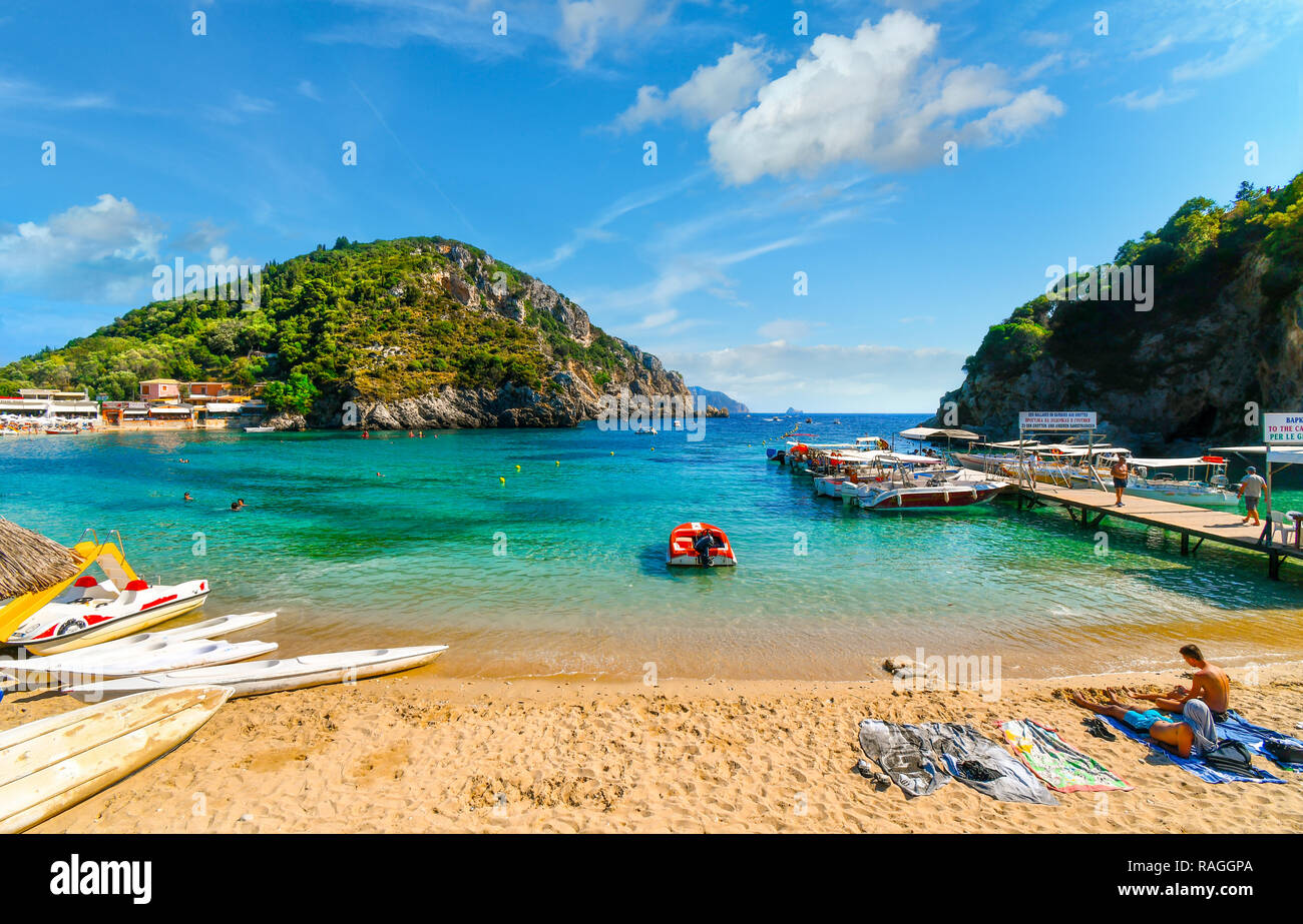 Touristen, die sich in der klaren Wasser und am Sandstrand von Palaiokastritsa Strand und Bucht in der Nähe der Bootsanlegestelle an der Ägäischen Insel Korfu, Griechenland. Stockfoto