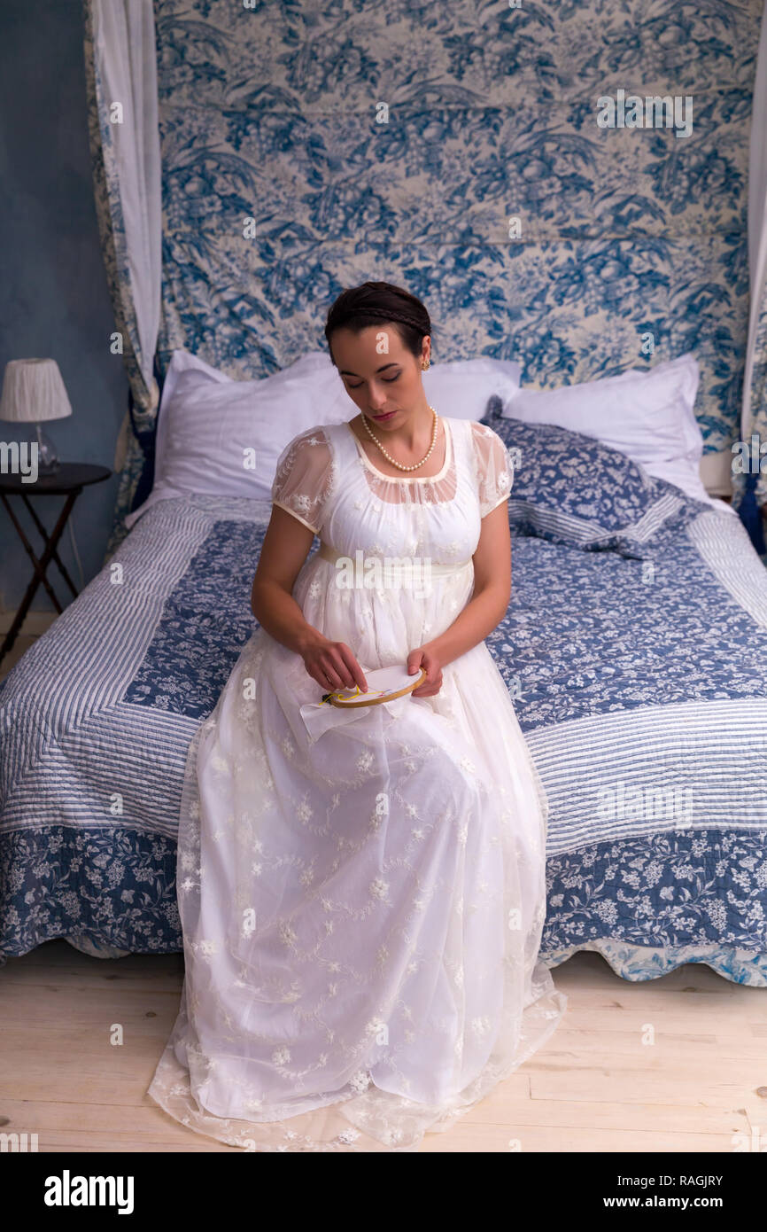 Attraktive junge Frau in authentischen Regency Kleid sitzt auf einem antiken Bett Stockfoto