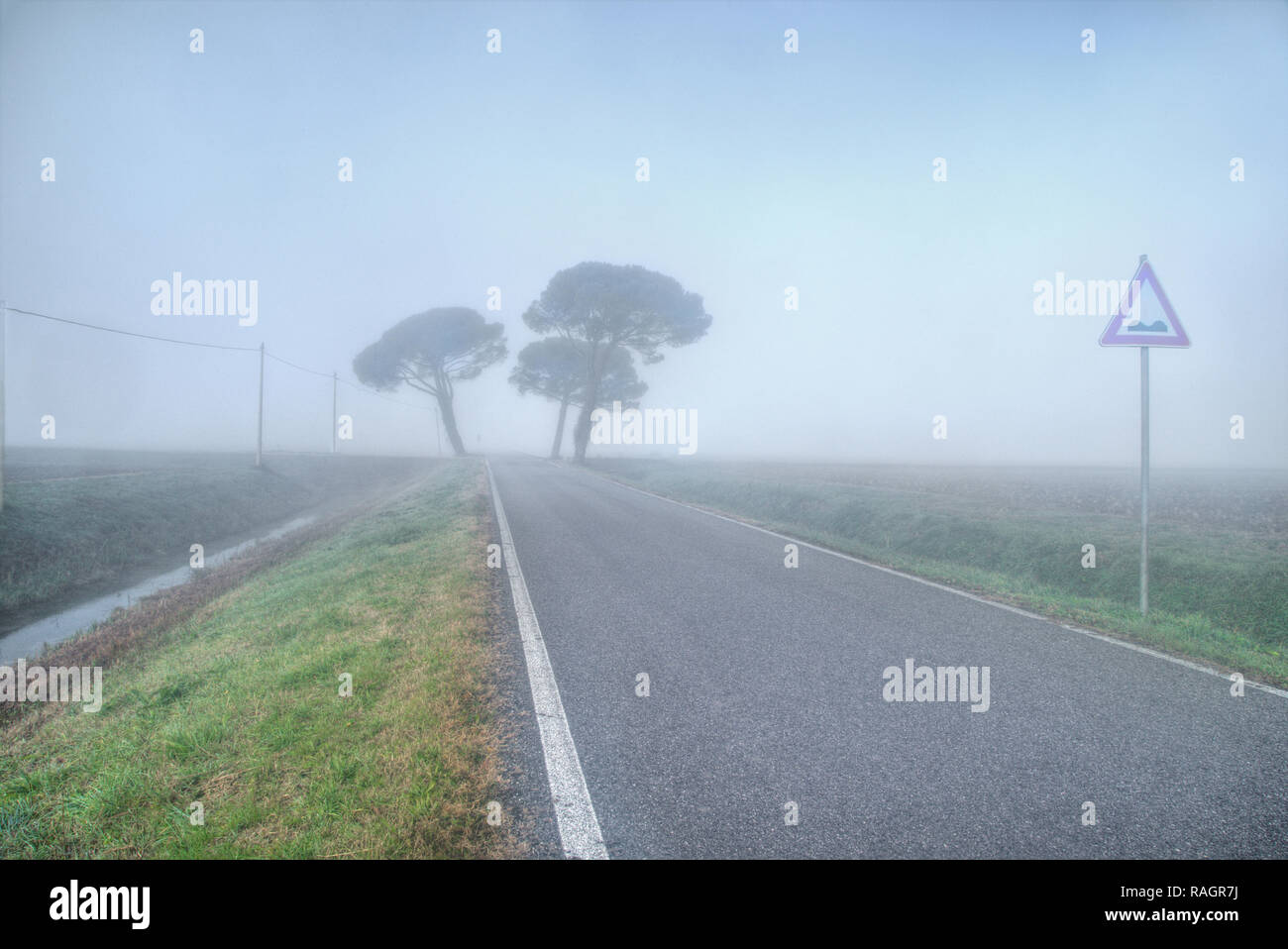 Ländliche Straße mit verkehrsschild im dichten Nebel, Grado - Italien Stockfoto