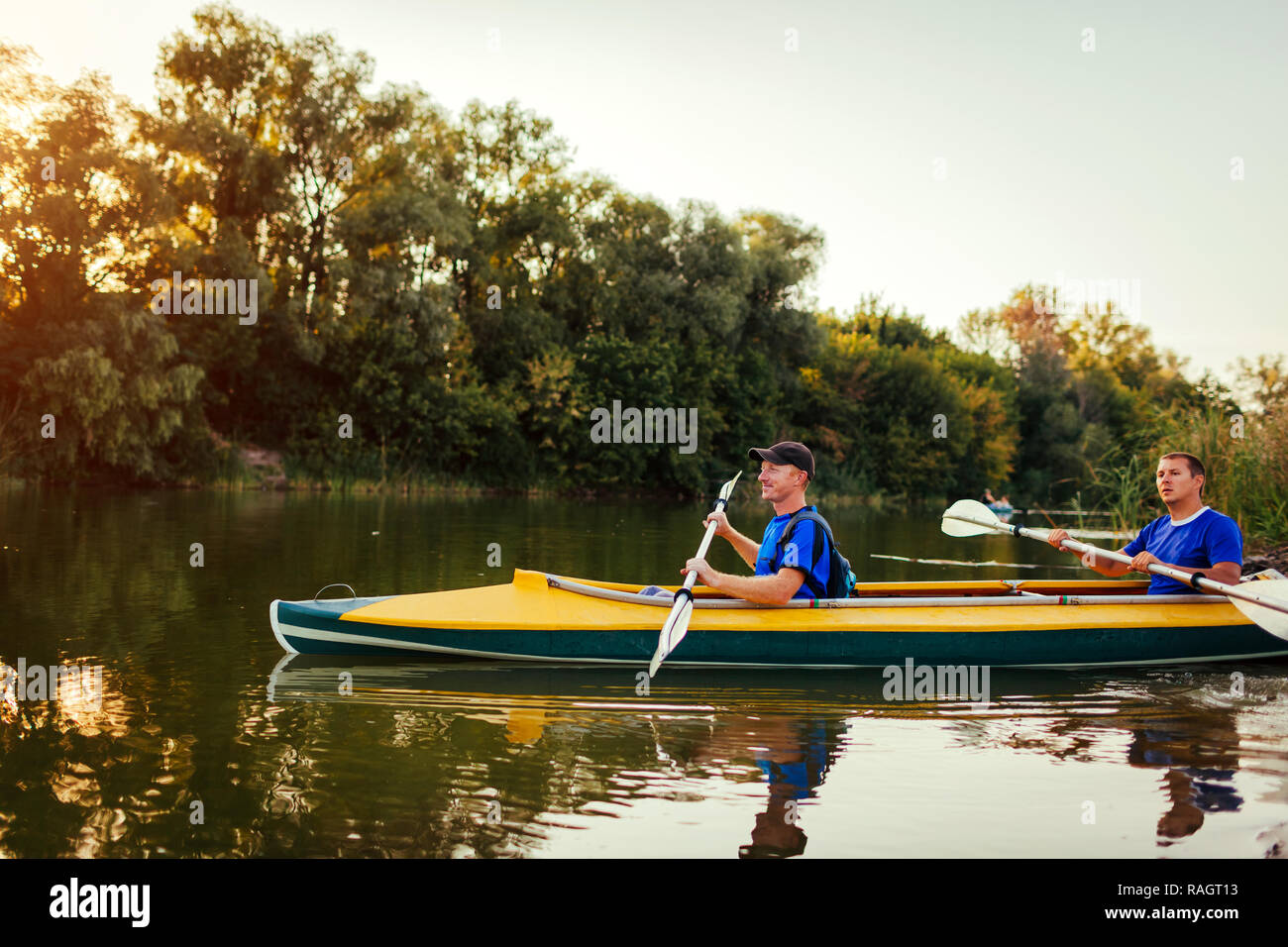 Junge Männer rudern Kajak auf dem Fluss bei Sonnenuntergang. Paar Freunde Spaß Kanu im Sommer Stockfoto