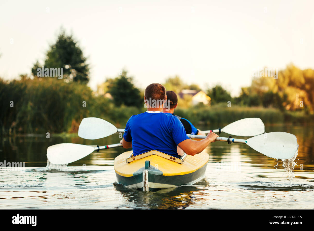 Junge Männer rudern Kajak auf dem Fluss bei Sonnenuntergang. Paar Freunde Spaß Kanu im Sommer Stockfoto