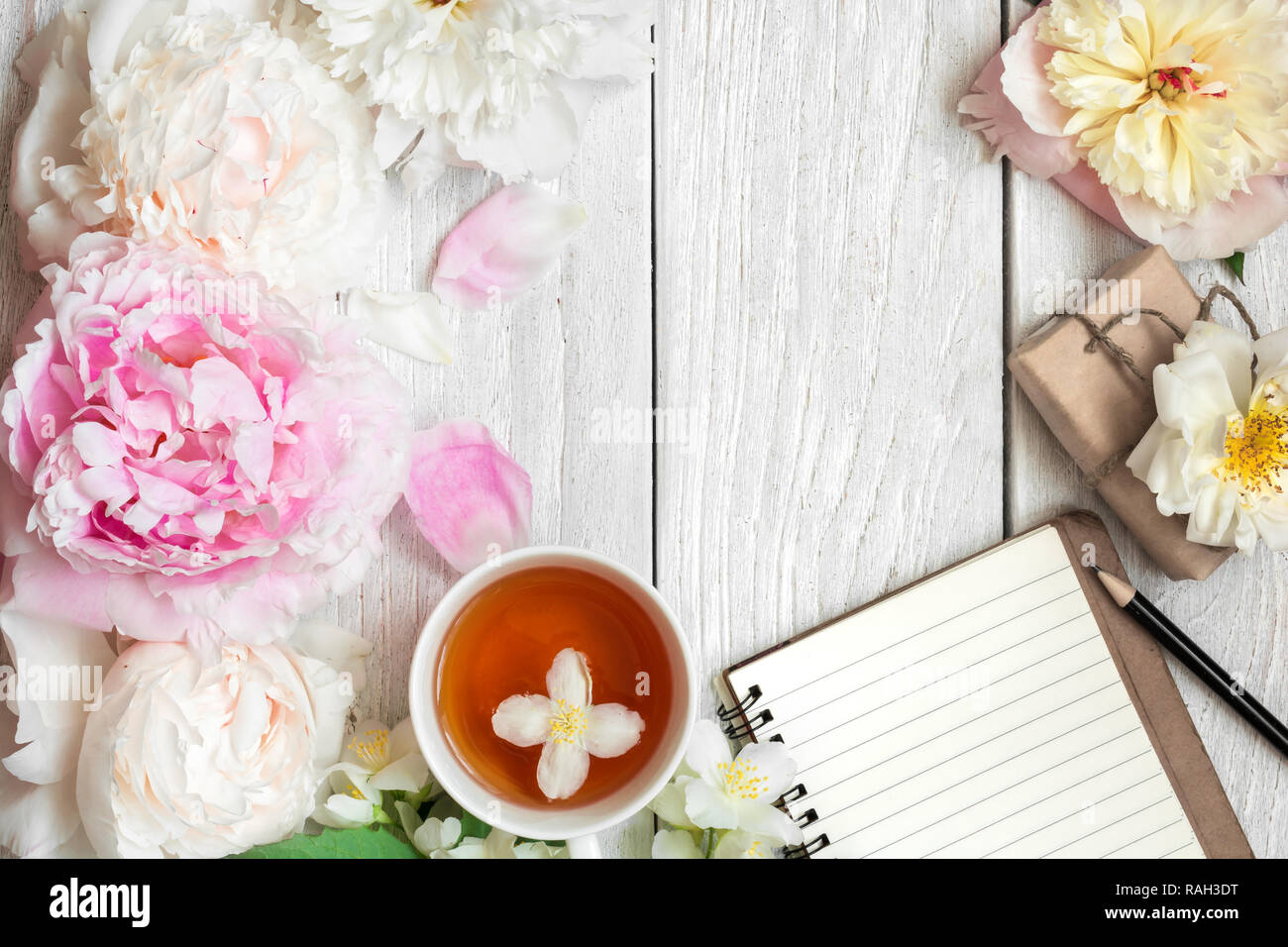 Festliche Komposition. Tasse Tee mit Pfingstrose, Rose und Jasmin Blüten mit Geschenkbox und Notebook. Flach. top View Stockfoto