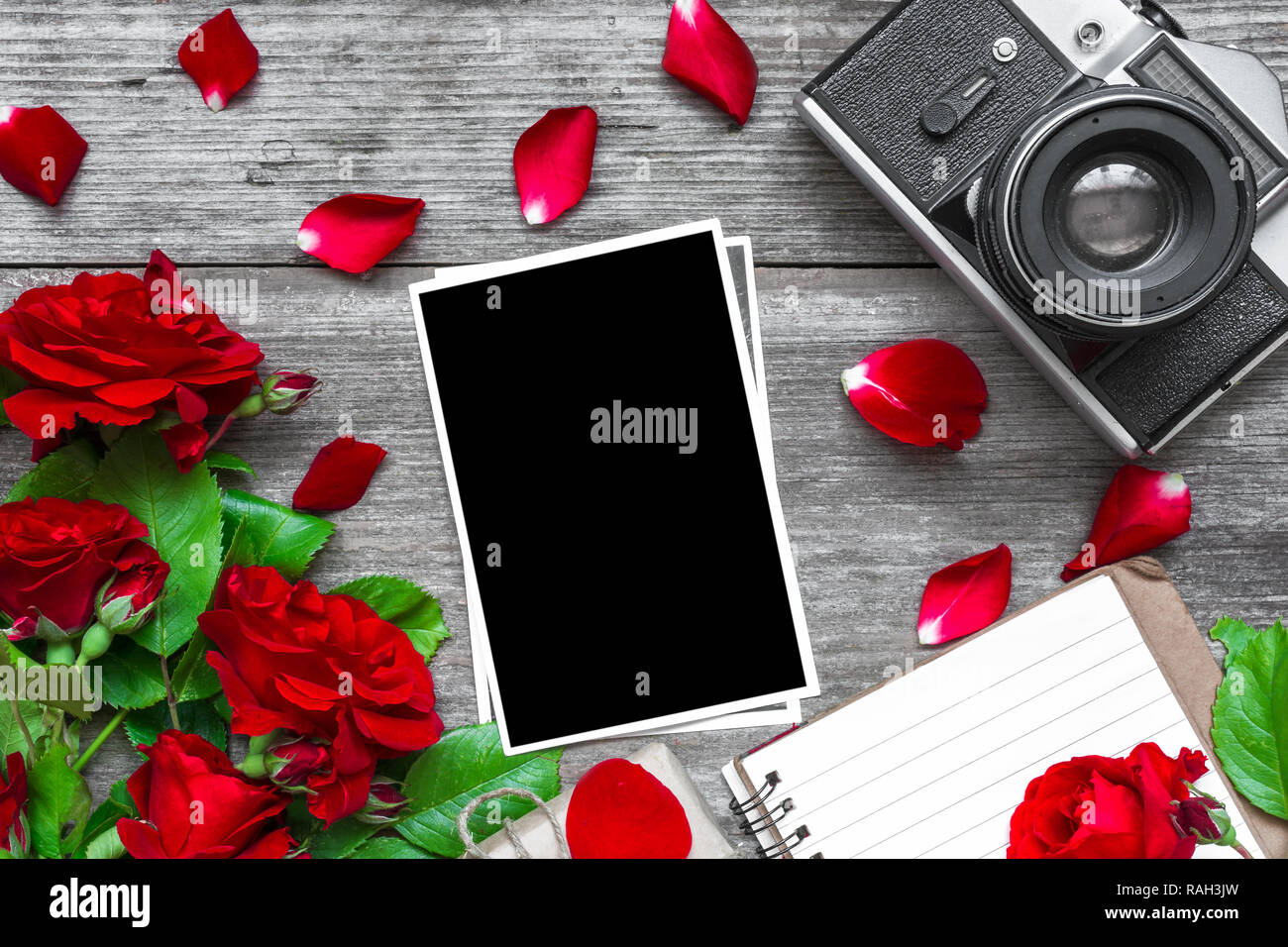Vintage Retro Kamera und leeren Bilderrahmen mit rote Rose blumen blumenstrauss und gefütterte Notebook mit rustikalen Holzmöbeln Hintergrund. top anzeigen. Mock up. Flach. Stockfoto