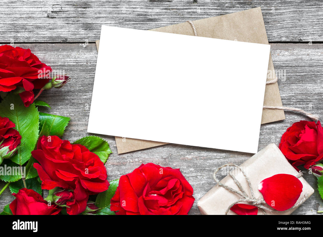 Leere weiße Grußkarte mit rote Rose blumen blumenstrauss und Umschlag mit Geschenkbox mit rustikalen Holzmöbeln Hintergrund. top anzeigen. Mock up. Flach. valentine Stockfoto