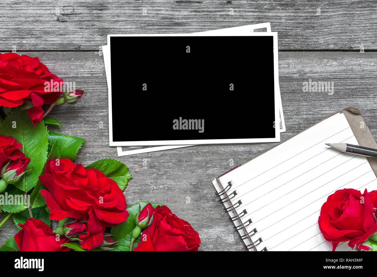 Leeren Bilderrahmen mit rote Rose blumen blumenstrauss und gefütterte Notebook mit rustikalen Holzmöbeln Hintergrund. top anzeigen. Mock up. Flach. Valentines Tag Hintergrund Stockfoto