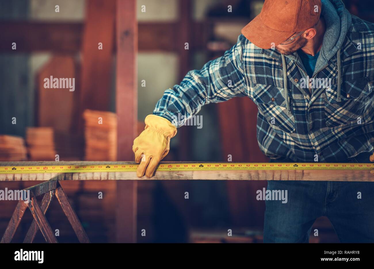 Kaukasische Arbeiter in seinem 30s Messen Holzbalken mit Maßband. Stockfoto