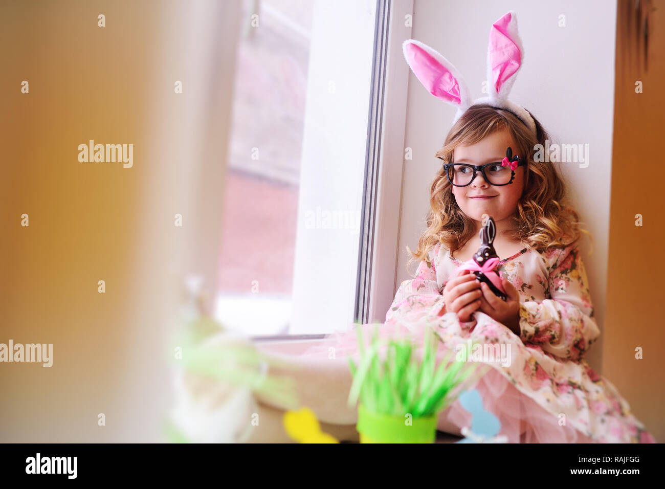 Baby schön Mädchen in einem smart Kleid mit Hasenohren auf ihrem Kopf Holding eine Schokolade Osterhasen Stockfoto