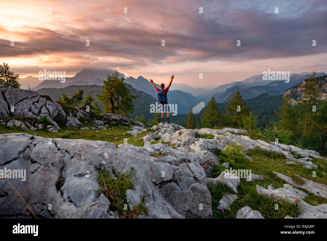 Wanderer seine Arme in die Luft streckt, Gipfeltreffen der Feldkogel, Blick auf den Königssee bei Sonnenuntergang, links Watzmann Südspitze und Stockfoto